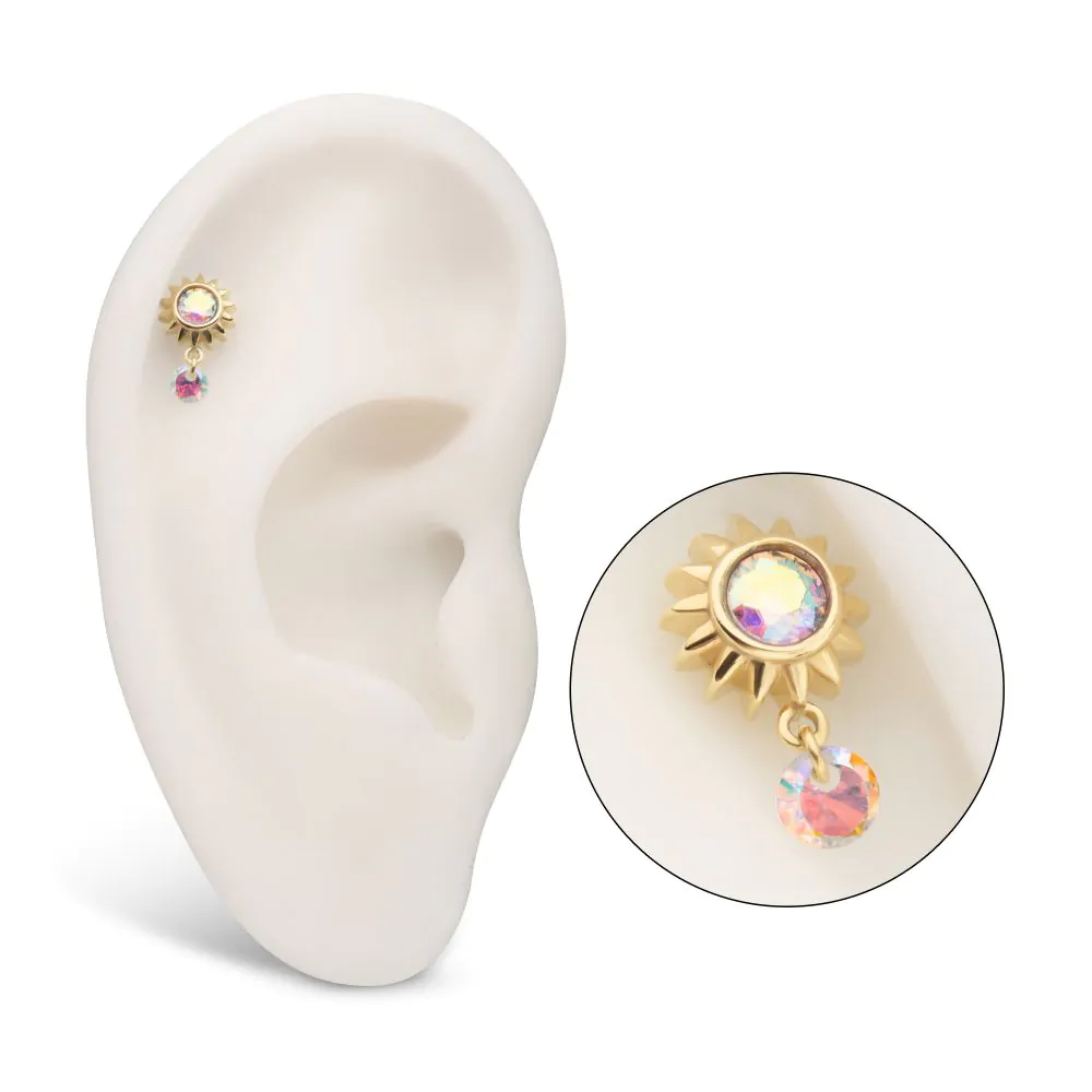 A 14k gold-colored sunburst-shaped body jewelry with a dangle design, featuring a multicolored gemstone in the center, and a second gemstone hanging from the jewelry. Shown on display in a model ear.