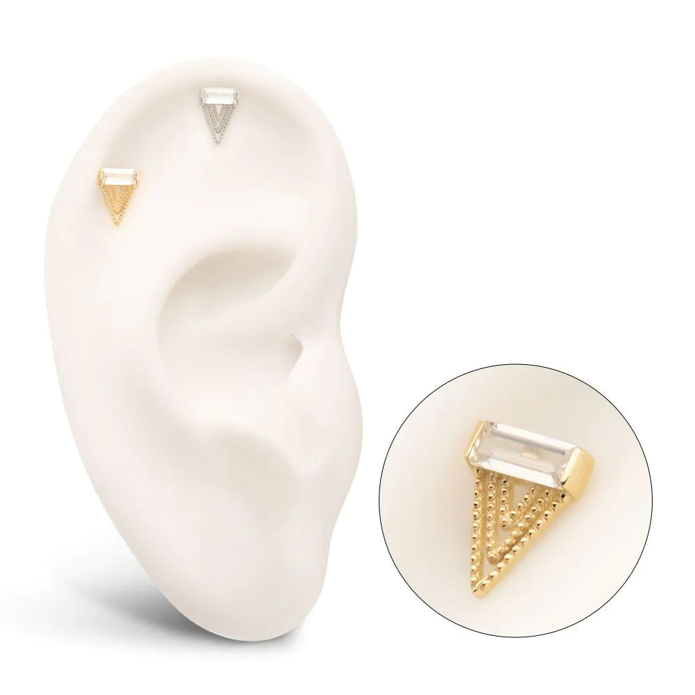 A triangular gold-colored body jewelry stud with a clear inset and intricate detailing, designed for use with a flatback post. Displayed in a model ear, with a close-up shot as well.