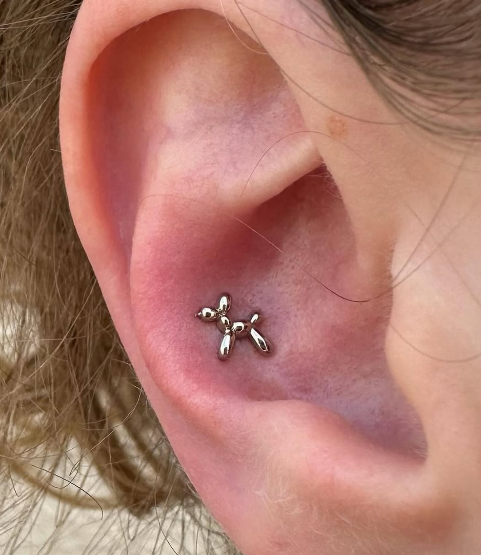 A close up of an ear with a balloon animal dog earring.