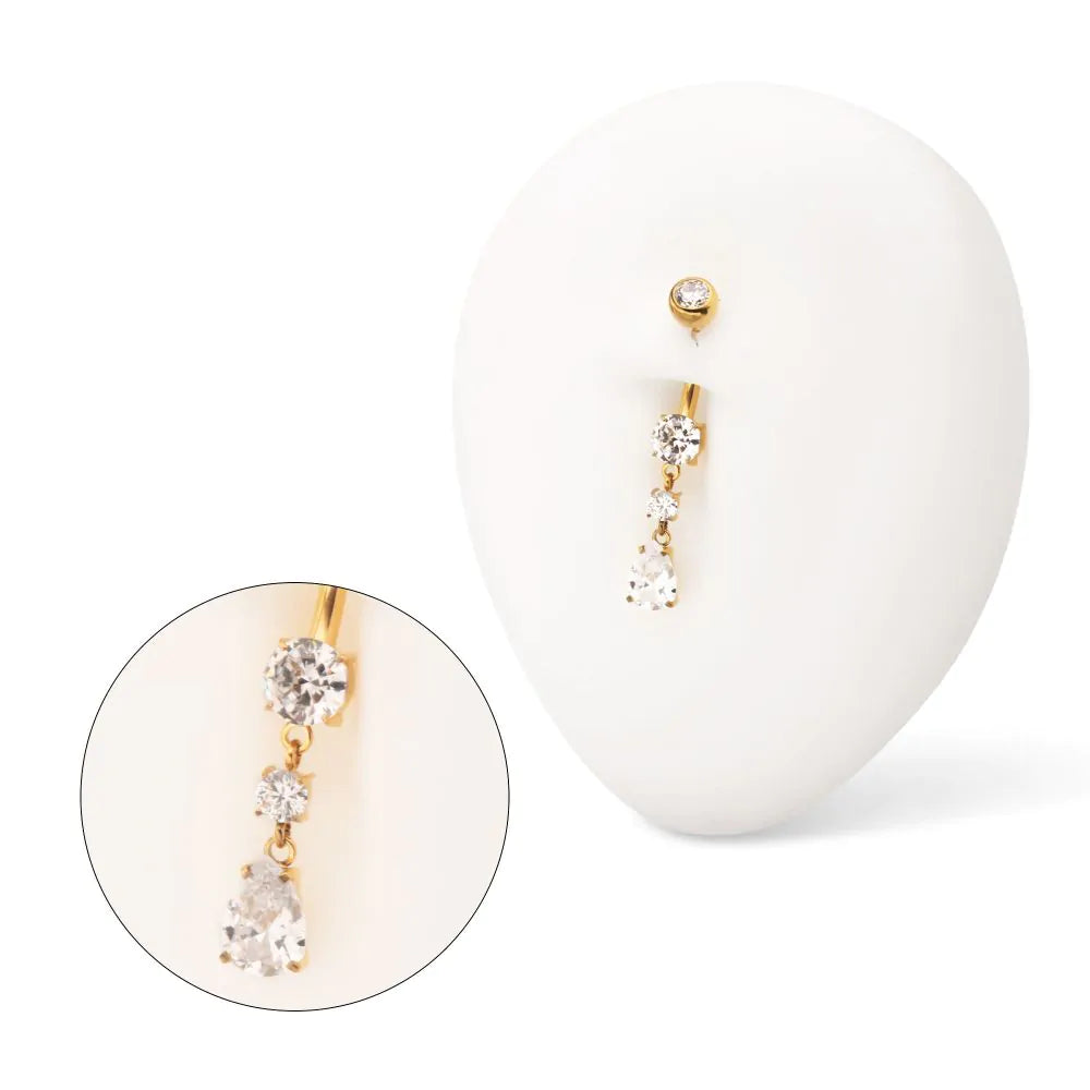 A gold-coloured navel barbell displayed in a white model navel.