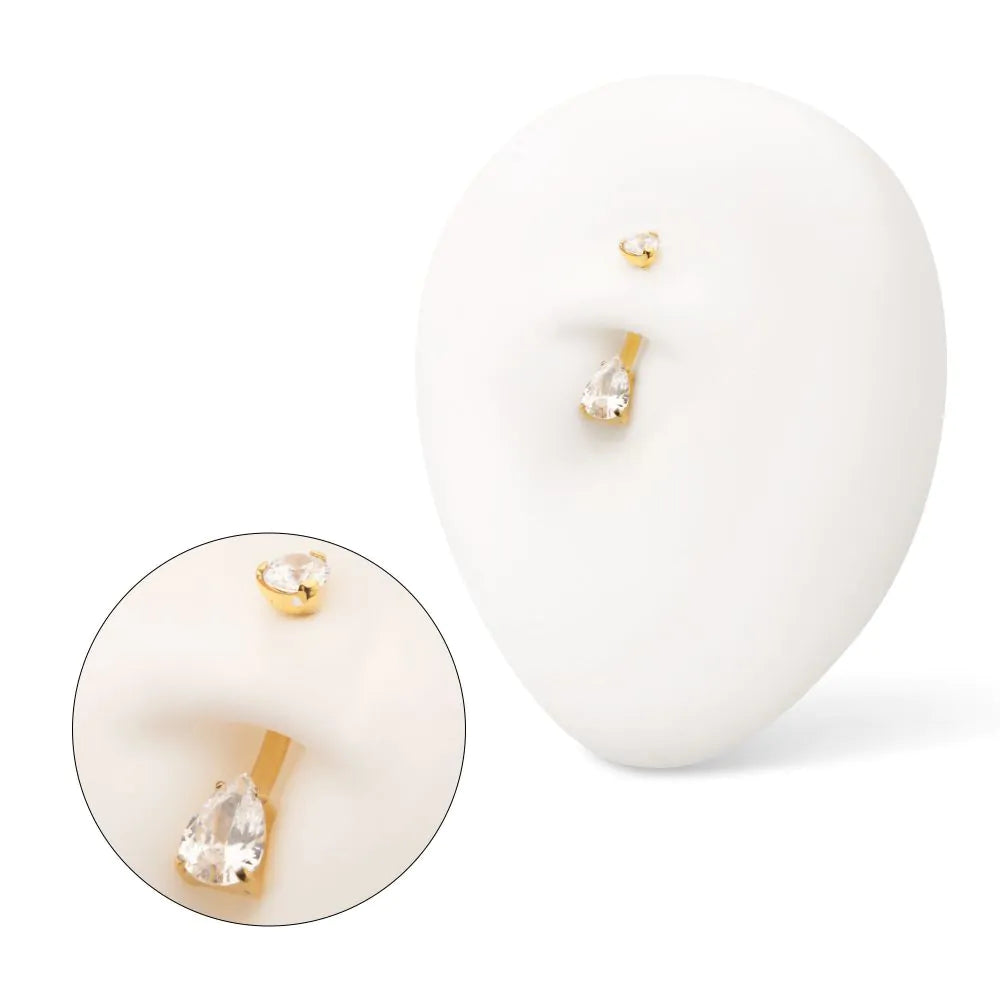 A gold navel piercing displayed in a white model navel, with a close-up shot as well.