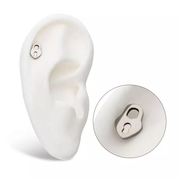 A silver heart-shaped locket with a keyhole on the front, shown on display in the helix piercing of a model ear.