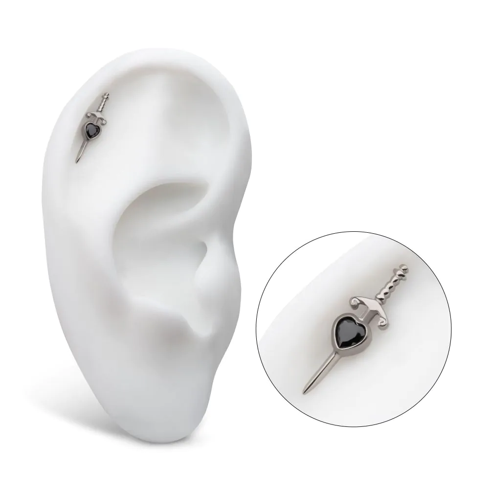 A titanium dagger piercing a black heart CZ, installed in the helix piercing of a model ear.